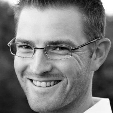 Black and white portrait of a smiling man wearing glasses with short dark hair